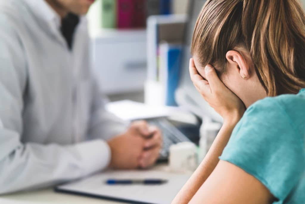 Young girl holding her head in her hands sitting at a desk with an adult.