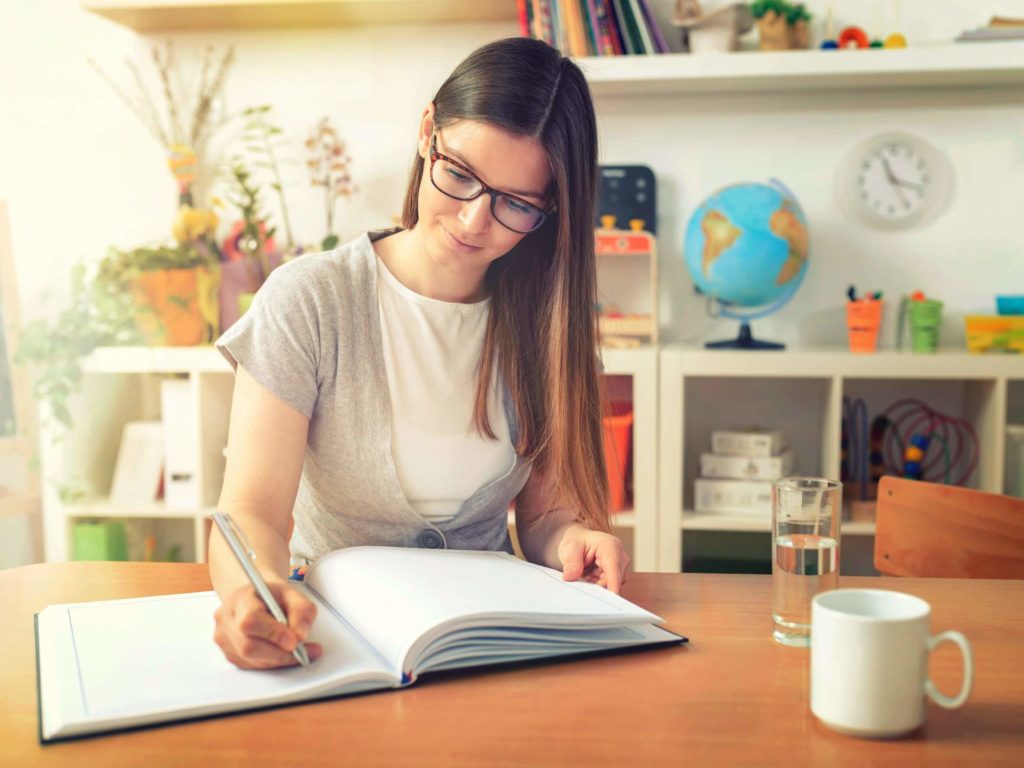A school teacher writes in a mark book in her classroom.