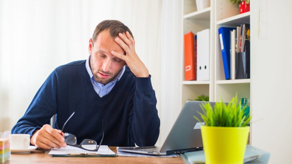 A man holds his head at his work desk in a stressed manner.