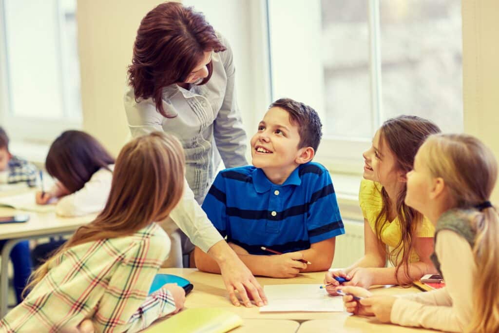 A teacher helps a smiling group of students as they work on an assignment.