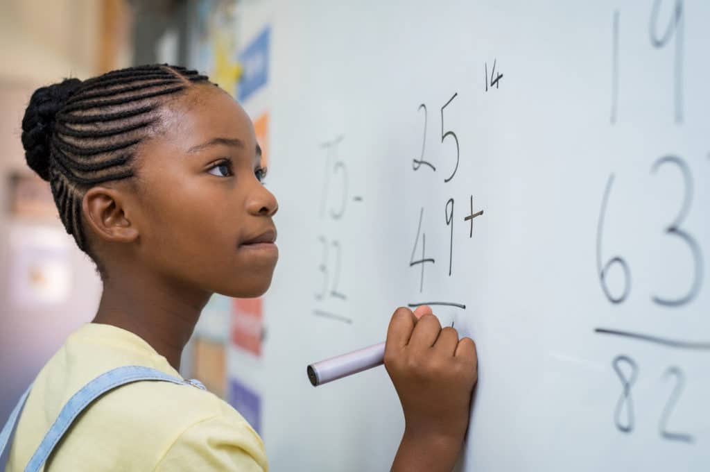 Young student working on math problems on a white board.
