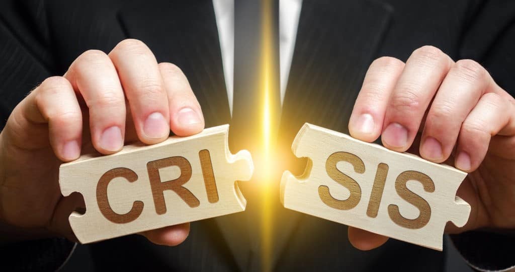 A man holding two puzzle pieces that fit together and read ‘crisis’.