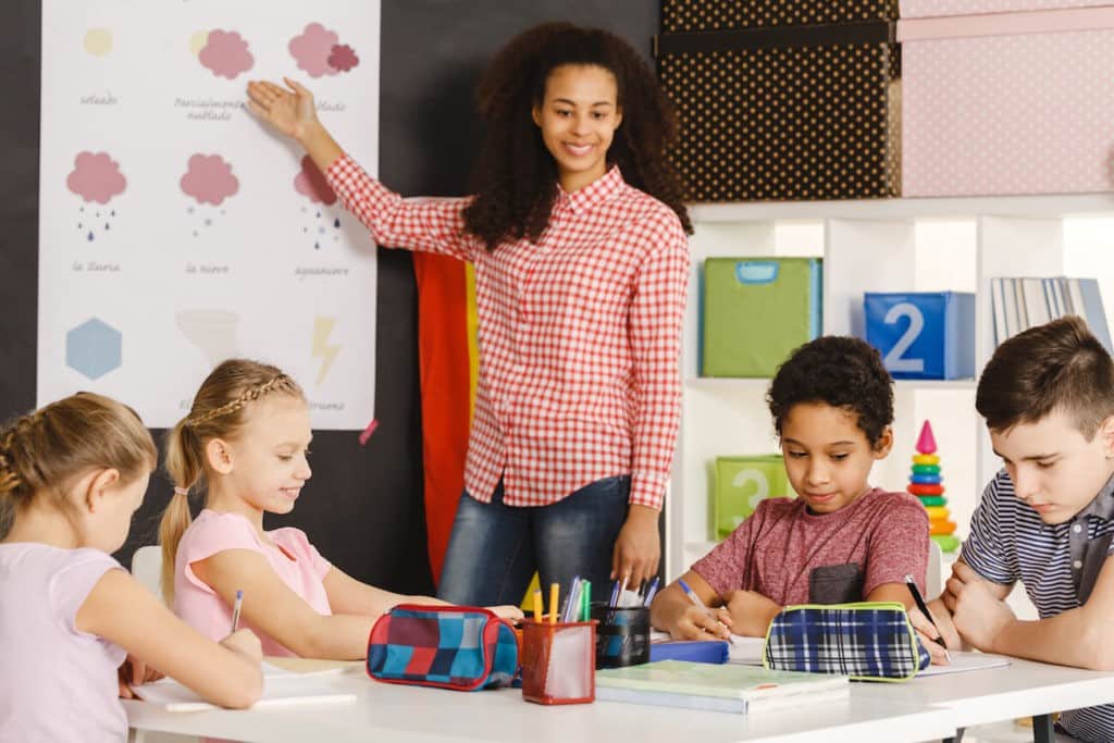 Teacher pointing out words about weather in Spanish to students.