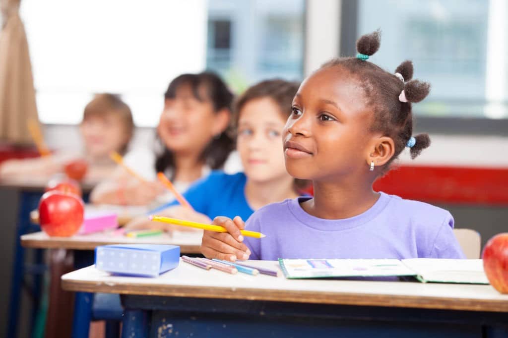 Young Black girl sitting at a desk looking inquisitively.