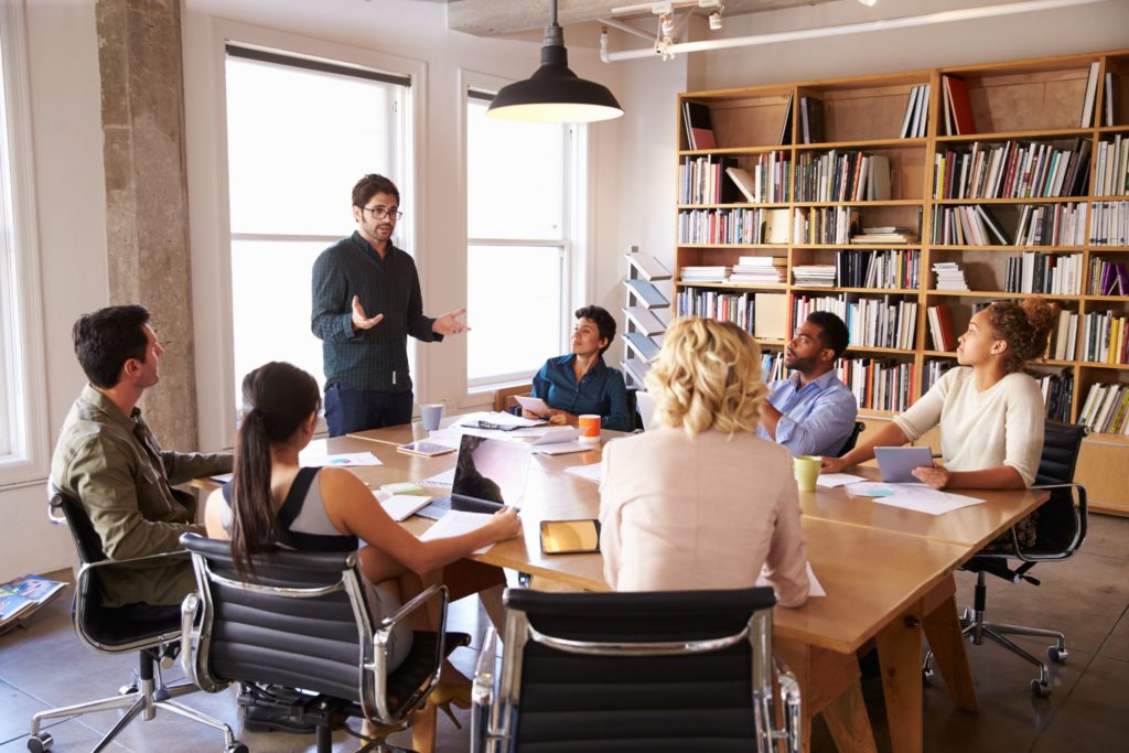 A group of professionals still around a table in a library, having a discussion.