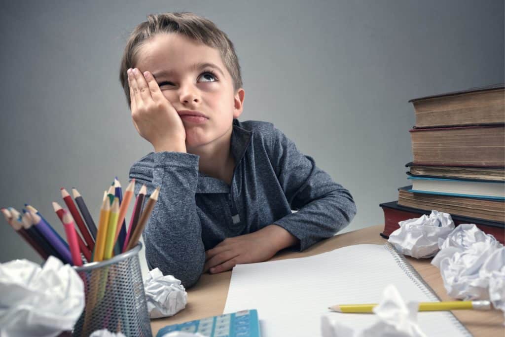 Young boy looking frustrated surrounded by school supplies.