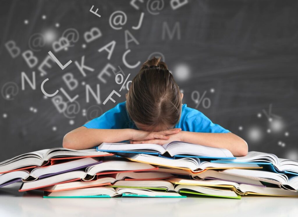 A girl sits in the classroom with her head on a pile of books, letters scattered in the air above her head, representing dyslexia and dyslexia fonts.