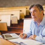 A teacher attends a college class and sits in a lecture hall.