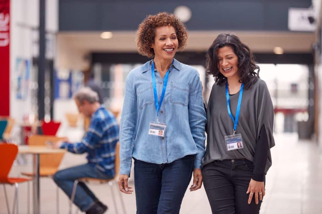 Two teachers walk together, laughing and smiling.