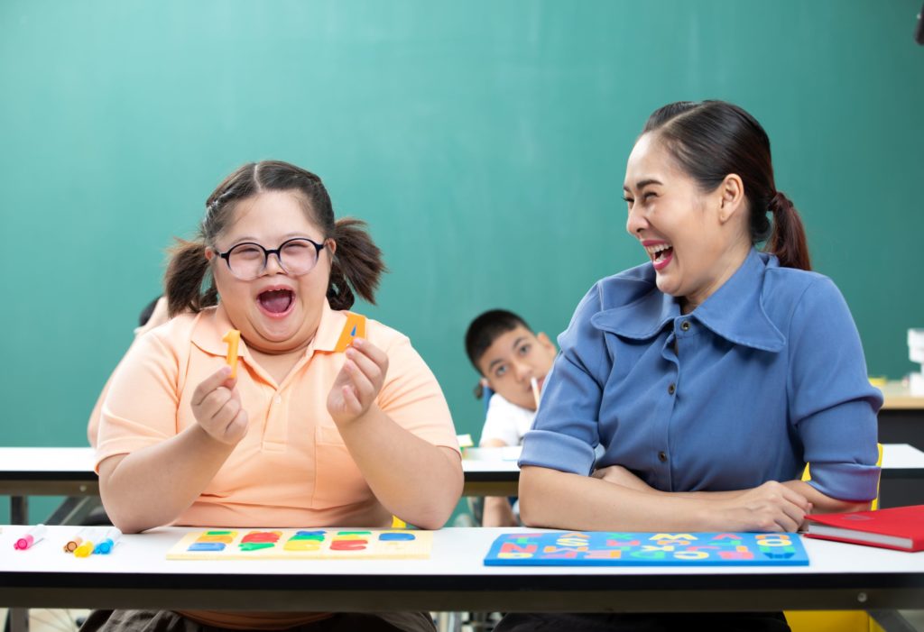 A teacher laughs with a special needs student.