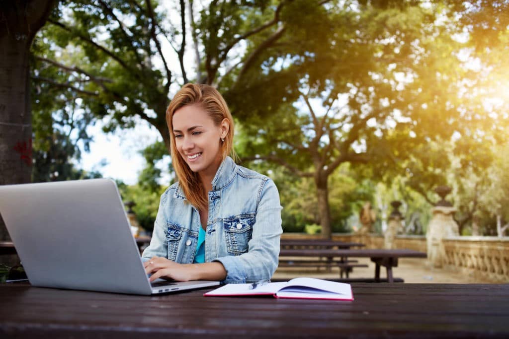 Young woman working on a laptop sitting outside.
