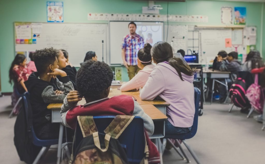Diverse group of students being taught by teacher at the front of the classroom.