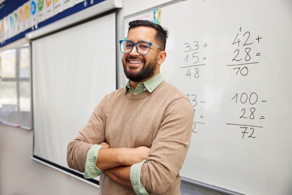 A math teacher stands in front of a whiteboard with math problems drawn on it.