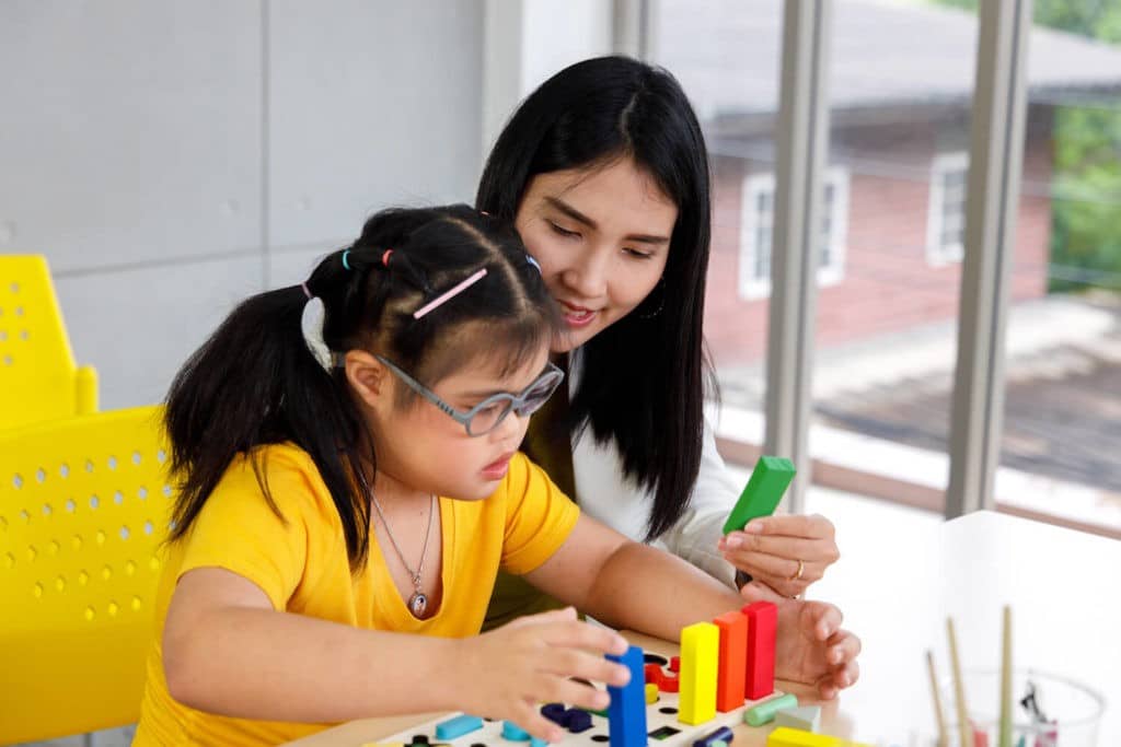 Special education teacher helping a young girl working with blocks.