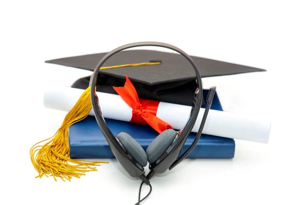 A diploma and master’s graduation hat sit next to a book and pair of headphones.