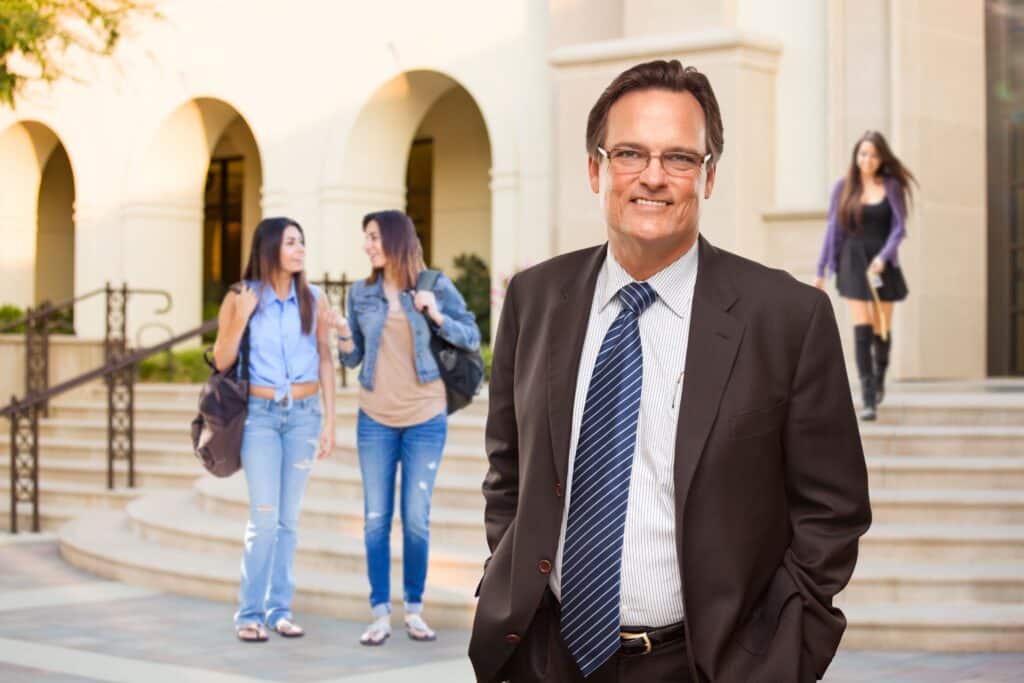 A male administrator stands in front of the school building.