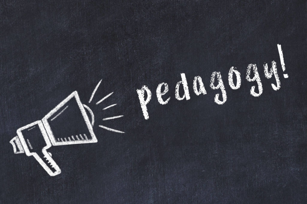 Chalk drawing of loudspeaker and handwritten word “pedagogy” on black chalkboard.