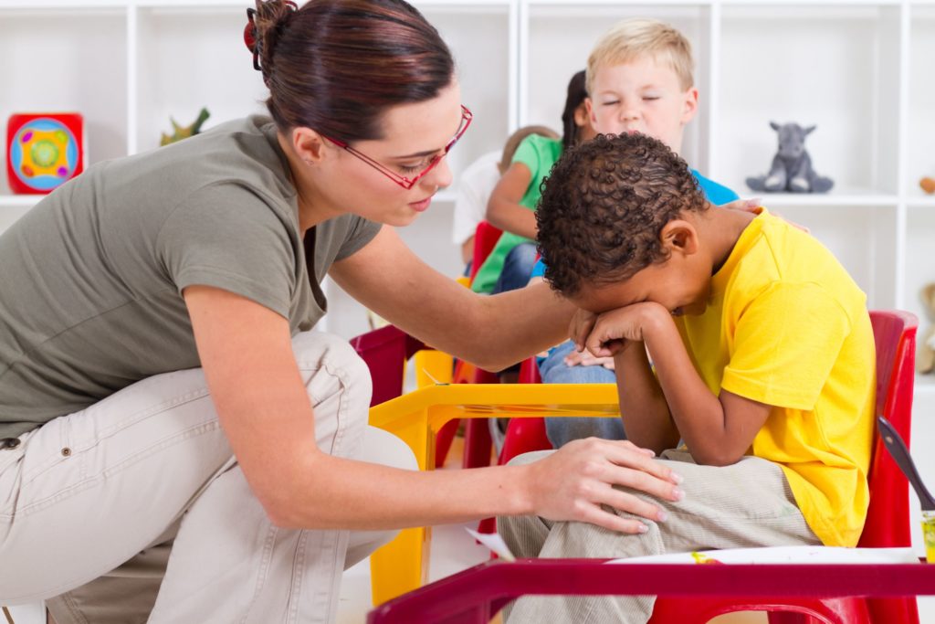 A teacher comforts a crying student in the classroom.