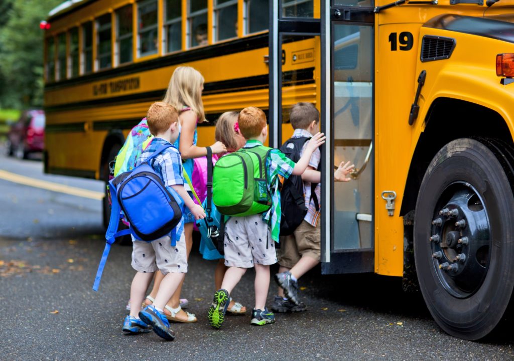 Group of young children with backpacks getting on a school bus.