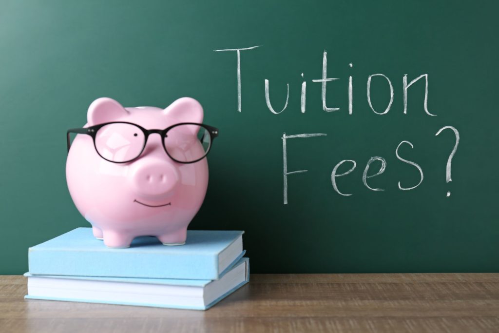 Piggy Bank on a desk with Tuition Fees? Written on chalkboard
