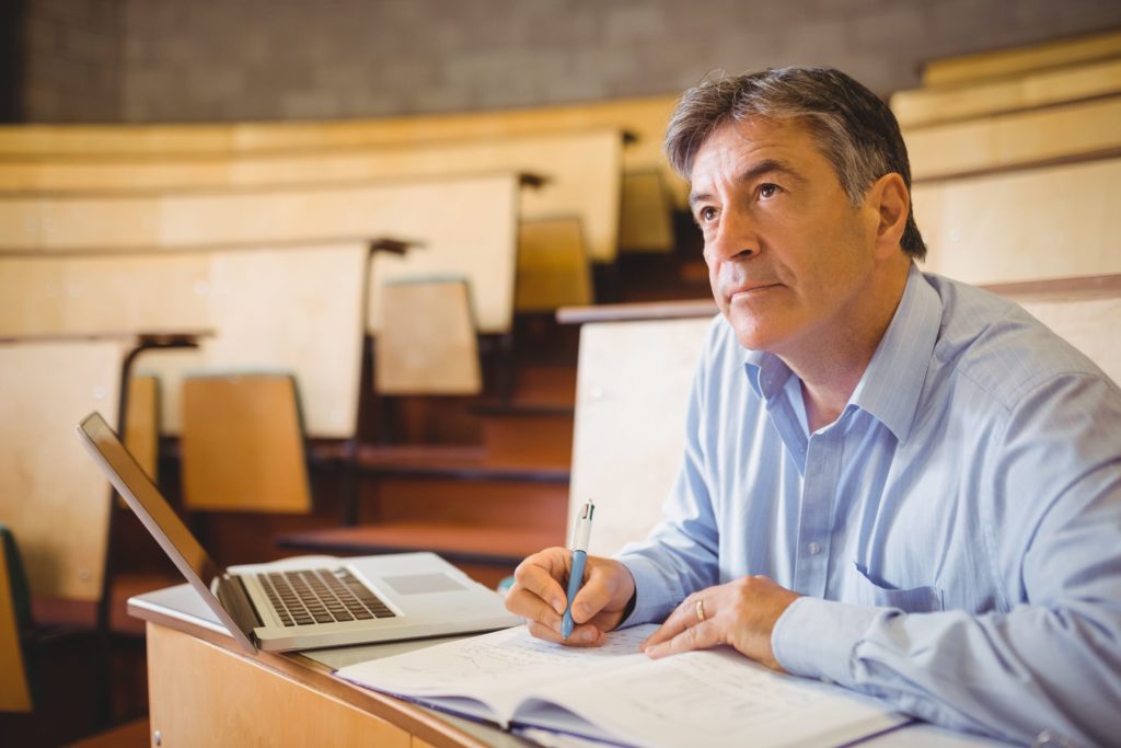 An older student sits in a lecture hall, taking notes.