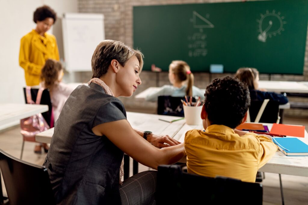 A paraprofessional helps an elementary school student in the classroom.