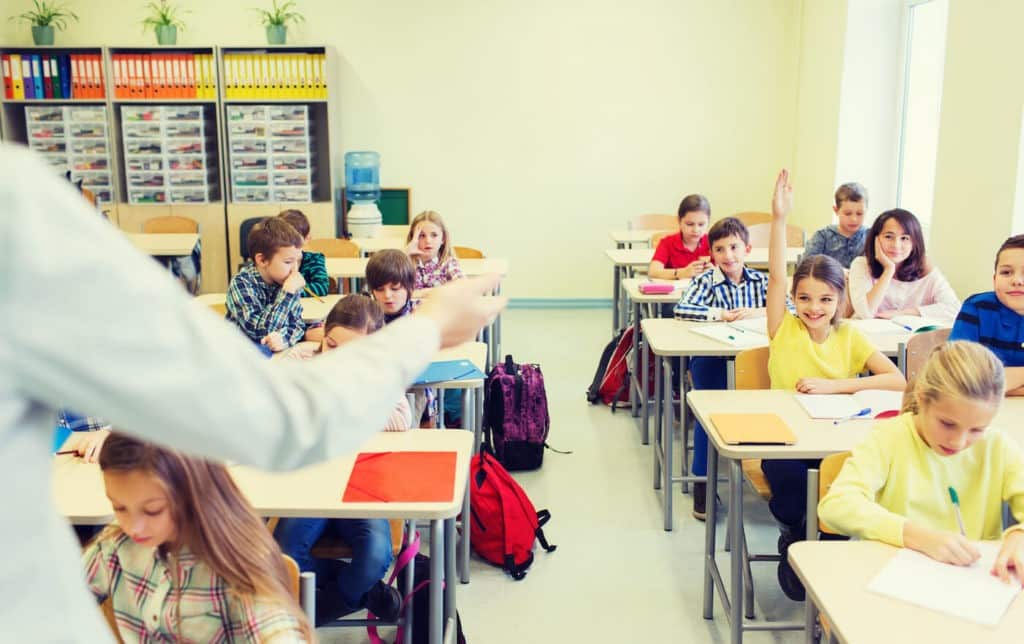 Teaching at the front of a classroom calling on a girl with her hand raised.