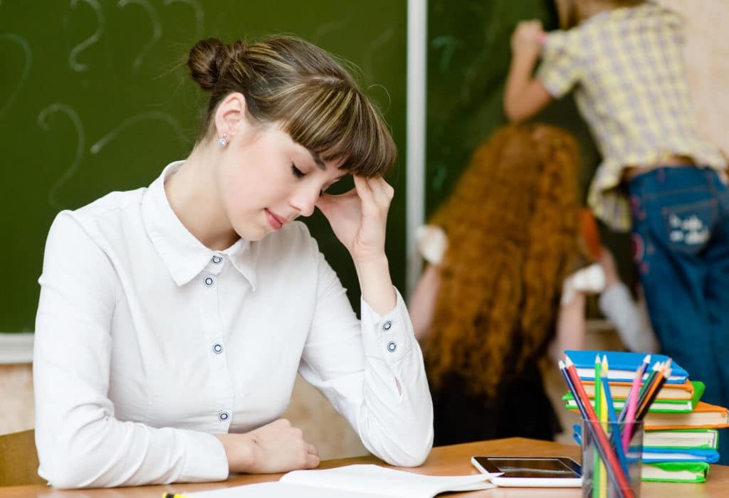 Female teacher pressing forehead to her hand and looking down at desk