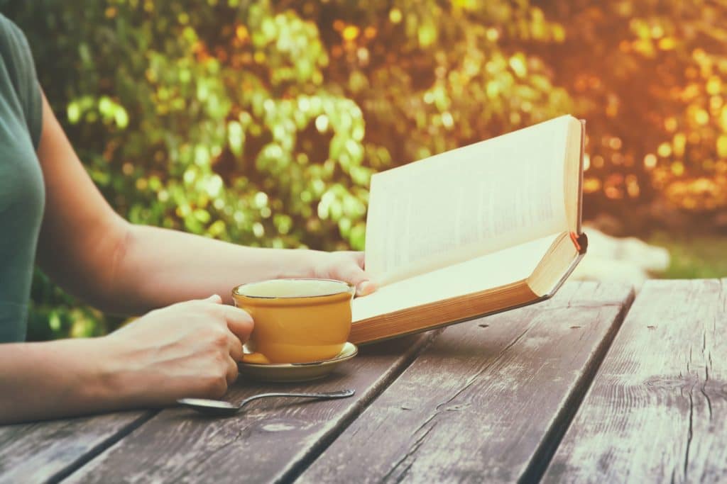 Close-up of a woman reading a book outside with a cup of coffee.