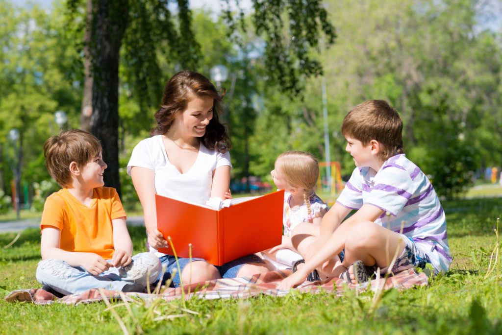 Two parents and their daughter read together outside on a picnic.