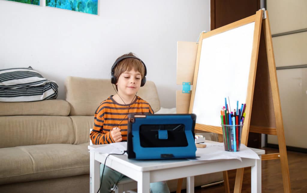 Young boy wearing headphones and watching a tablet next to a white board.
