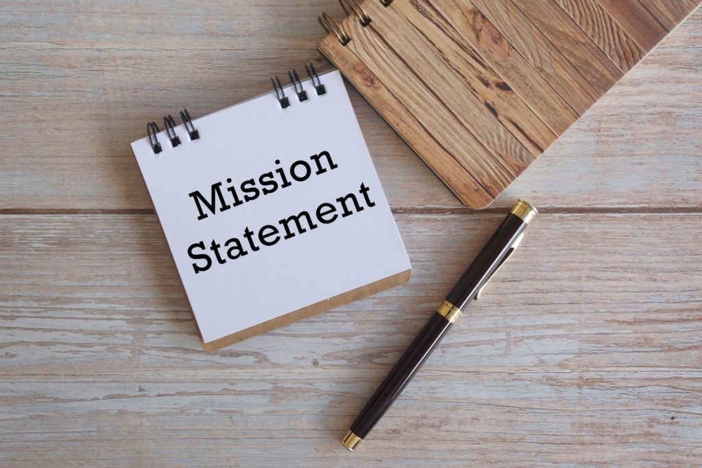 Notebook and pen on a wooden background with the words “mission statement” written out.
