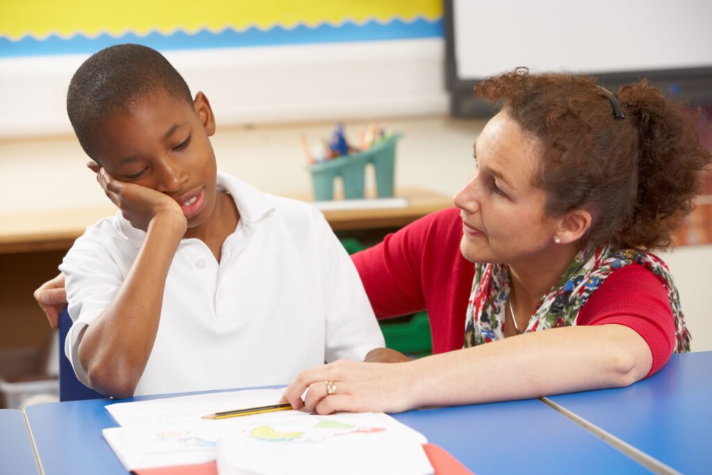 An upset boy studies with his teacher one-on-one in school.