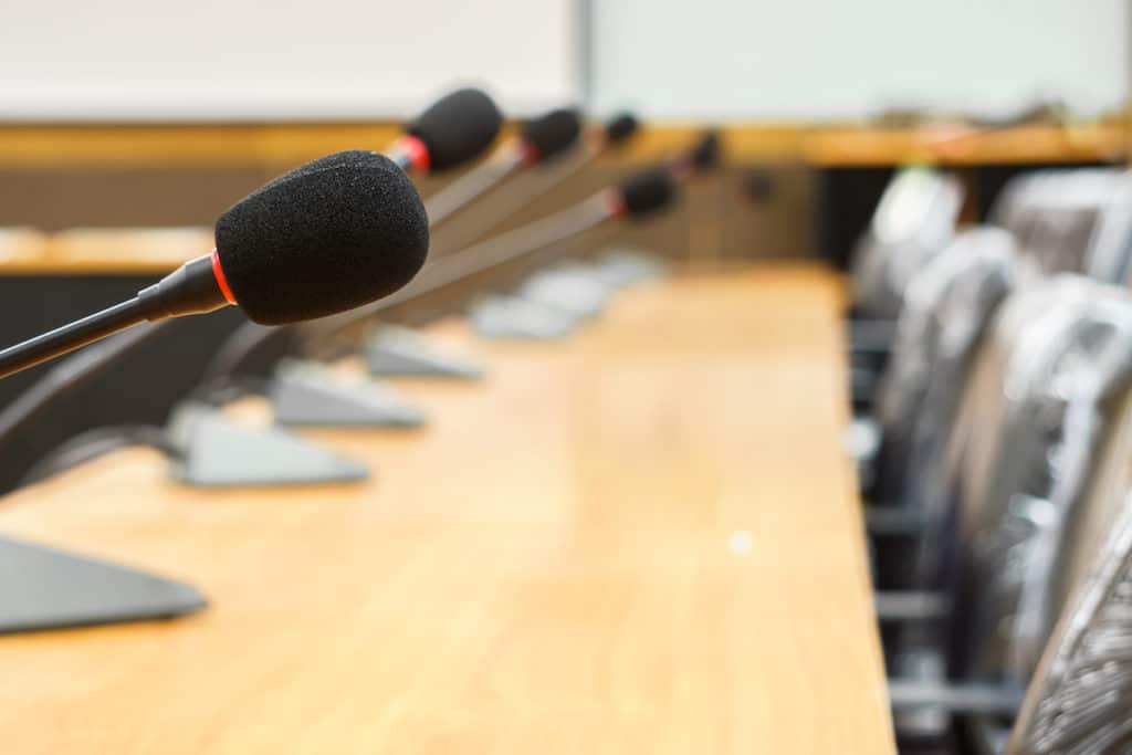 Long conference table with microphones and empty chairs lined up.