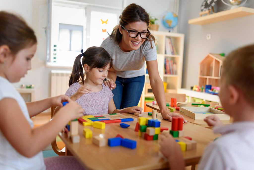Preschool teacher with children plays with young children and their colorful, wooden didactic toys.