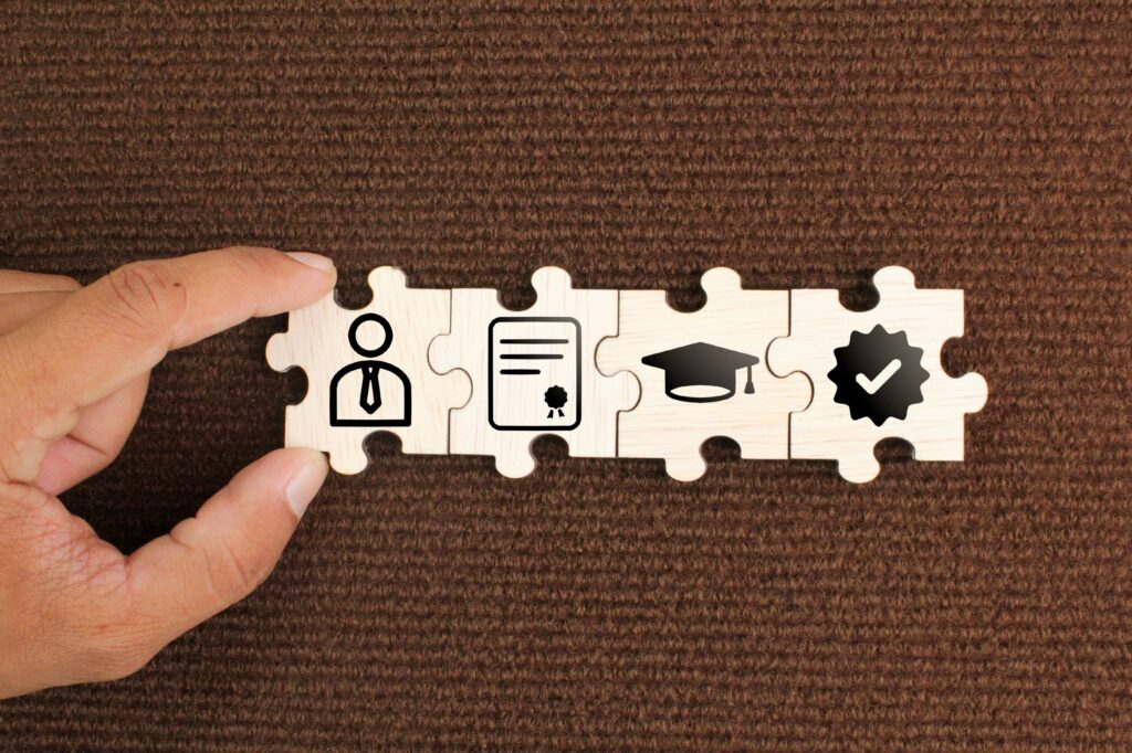 A man puts together a puzzle with a diploma, graduation cap, and checkmark.