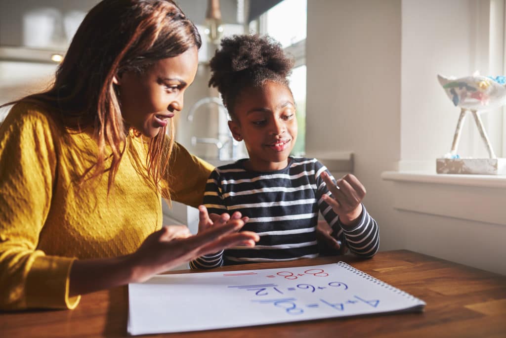 Mother sitting at a table with young daughter working on math problems.