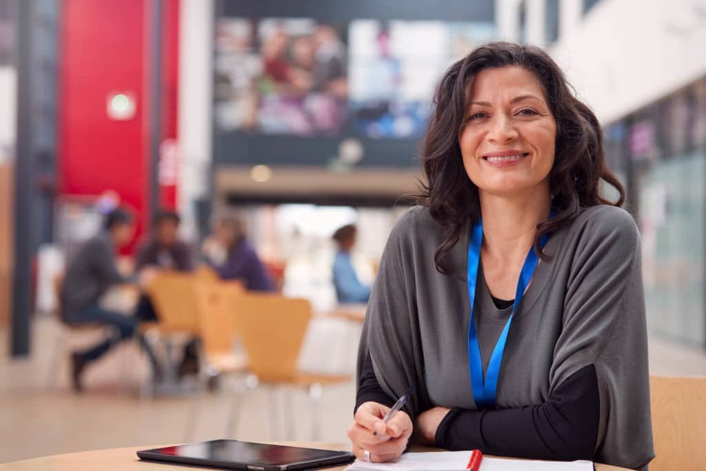 Older teacher sitting in a cafeteria working on papers.