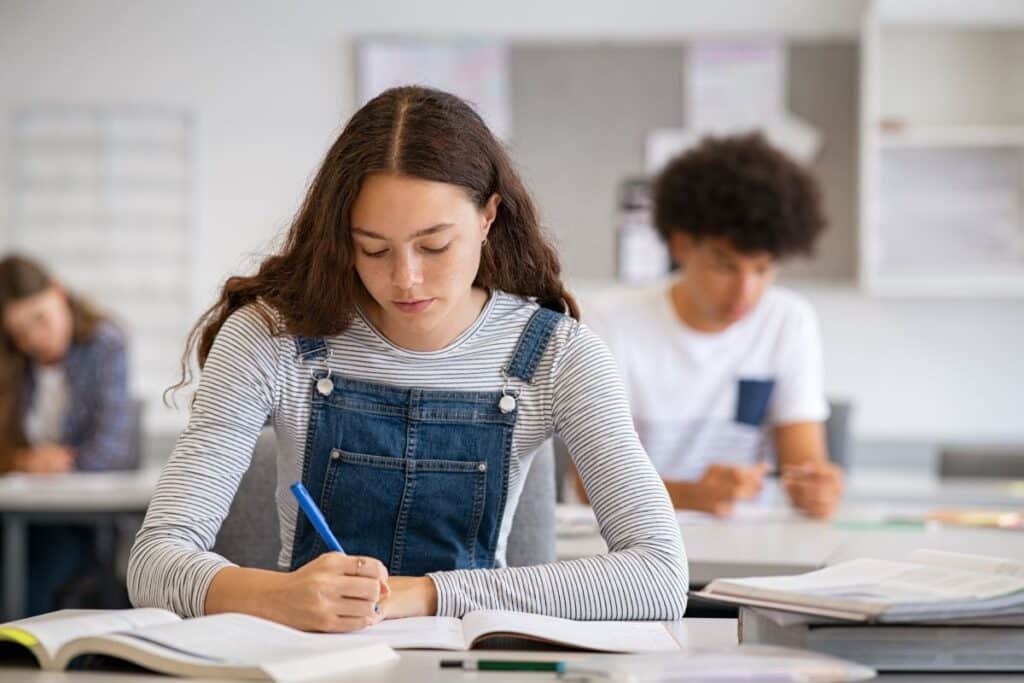 Creative writing prompts; a student sits in the classroom writing in her notebook.