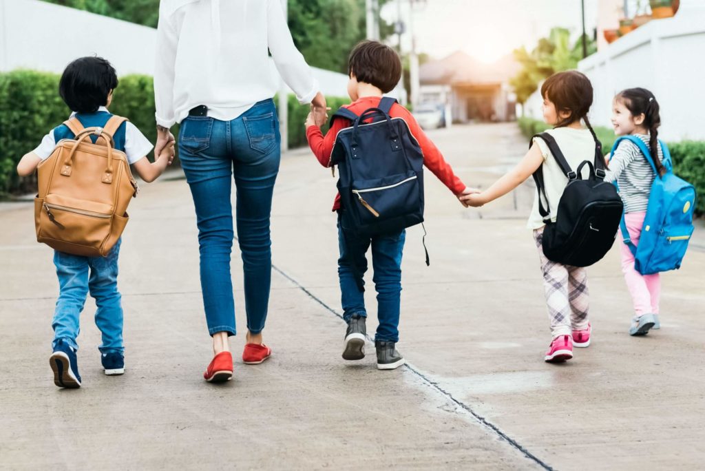 Teacher leads young students toward school entrance.