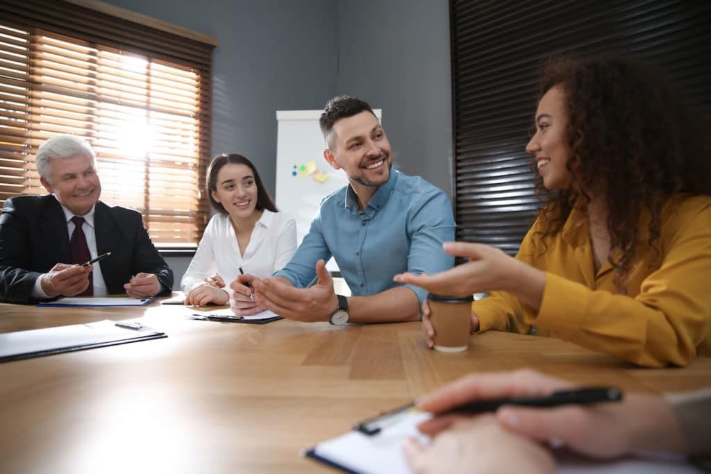 A group of professionals sit around a table in a meeting, laughing.