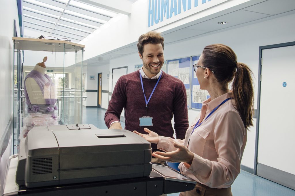 Two teachers talking at a copier machine.