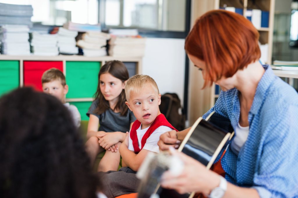 Teacher sitting playing guitar to a group of students with disabilities.