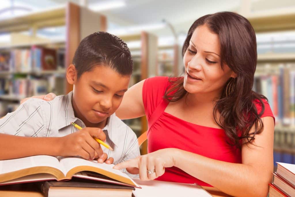 Teacher helping student with book in library.