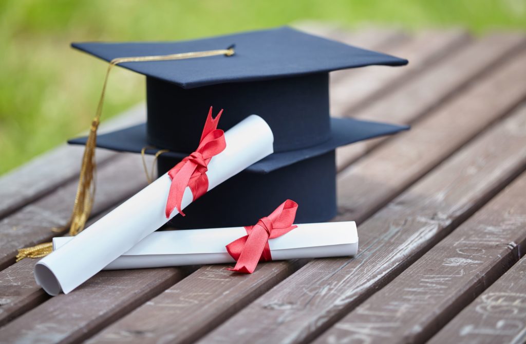 Two black graduation caps are stacked next to two diplomas.