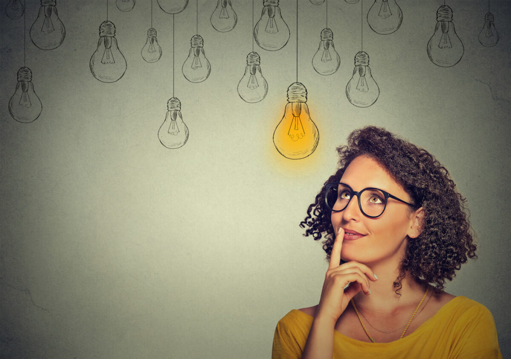Young woman thinking and standing in front on a chalkboard with light bulbs.
