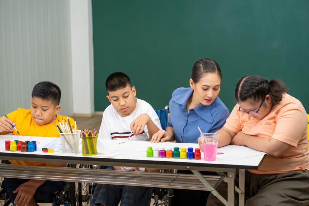 Female teacher sits and works with special needs students.