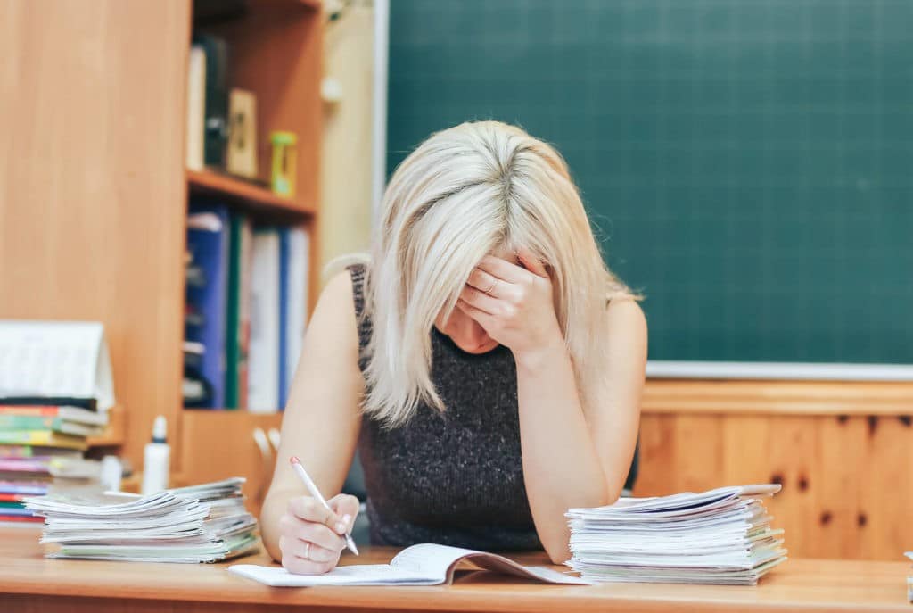Stressed teacher with her head down grading papers at her desk.