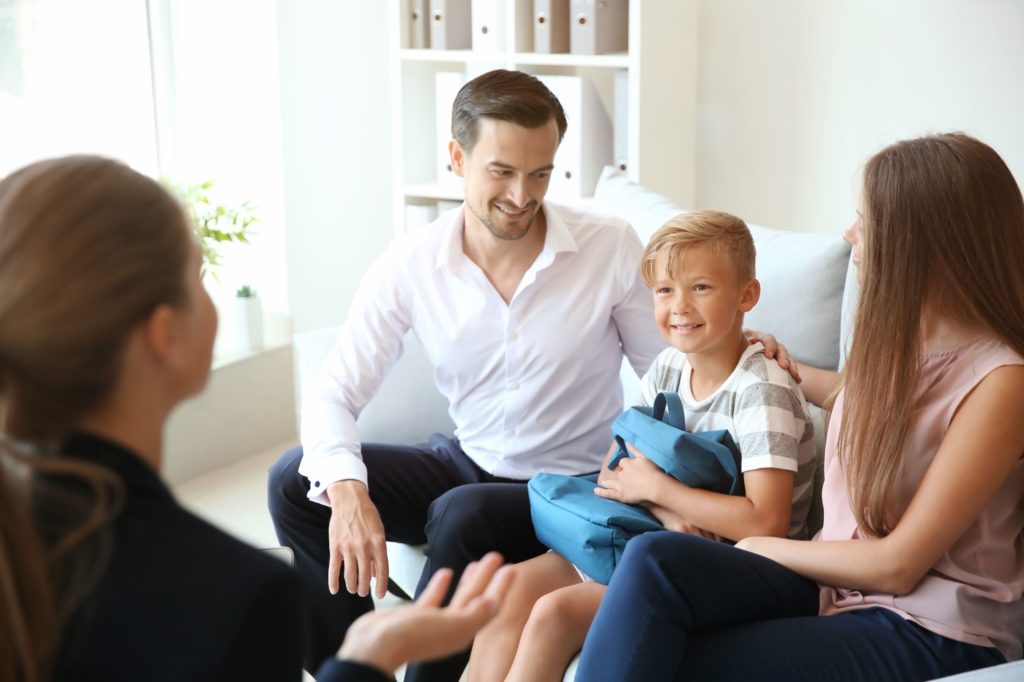 Parents sitting on a couch with their young son while talking to a teacher.