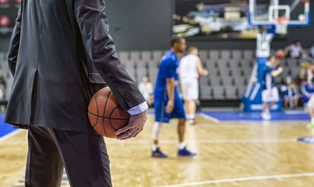 Basketball coach holds the ball in his hand, watching his team.